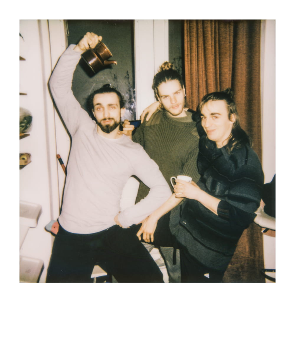 The three cofounders of StoryForgers posing in a kitchen, holding cups and a teapot, smiling in a casual, relaxed atmosphere.