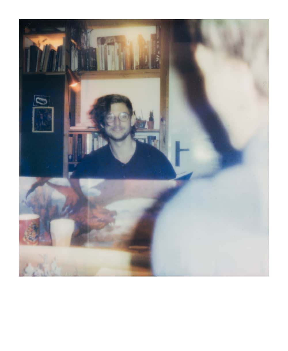 Double-exposure portrait of a smiling person seated in front of bookshelves